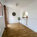 A bright room with wooden flooring, white walls, a wall-mounted decor item, a bar stool, and an arched opening to the kitchen. T. Samuel Estate Agents logo is visible.