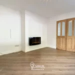Unfurnished room with light wood flooring, white walls, a wooden door, double glass-paneled doors, and a wall-mounted electric fireplace.