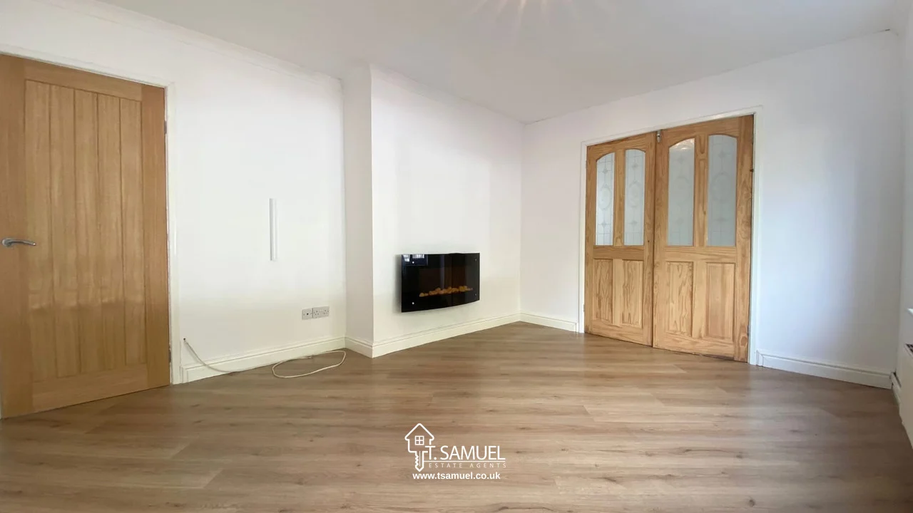 Unfurnished room with light wood flooring, white walls, a wooden door, double glass-paneled doors, and a wall-mounted electric fireplace.