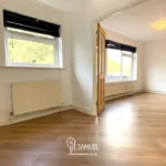 Bright, empty room with light wood flooring, white walls, large windows with black blinds, and a radiator beneath one window. Glass double doors lead to an adjacent room.