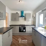 Modern kitchen with white cabinets, black countertops, built-in oven, gas stove, stainless steel hood, large windows, and wood flooring.