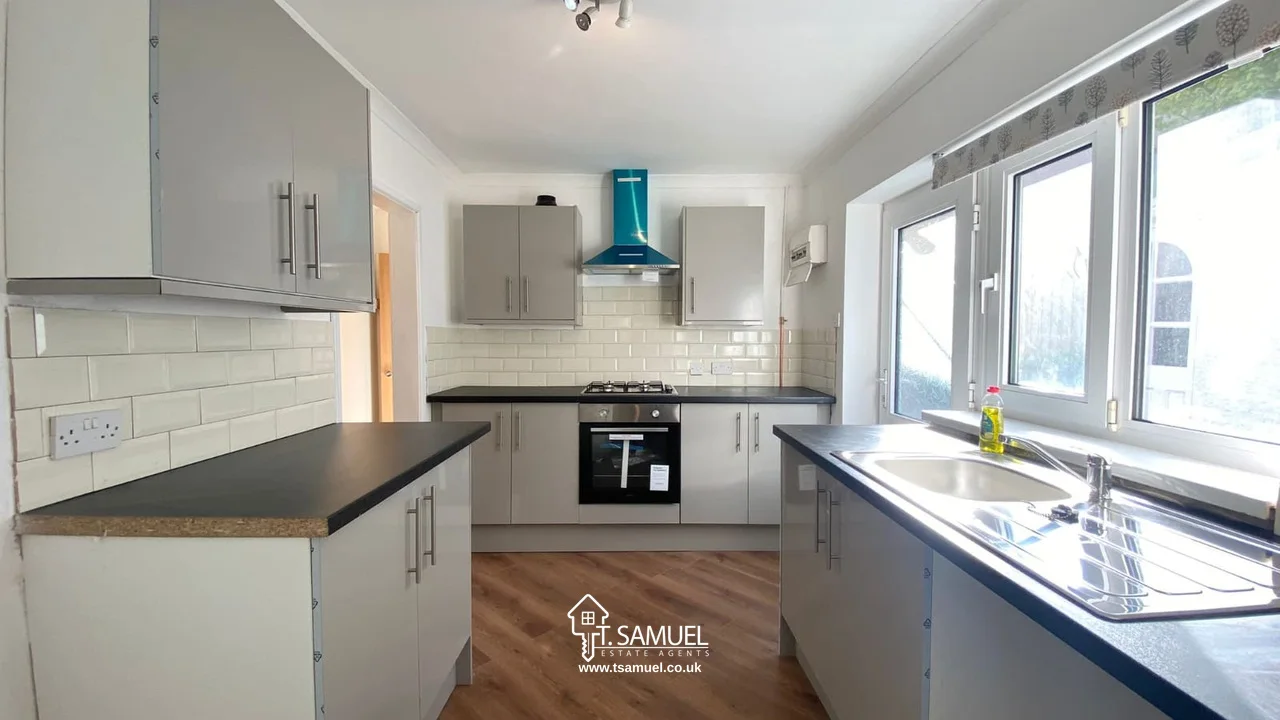Modern kitchen with white cabinets, black countertops, built-in oven, gas stove, stainless steel hood, large windows, and wood flooring.