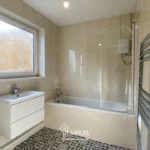 Modern bathroom with a bathtub and shower, a frosted window, white vanity with drawers, patterned floor tiles, and a towel radiator on the right wall.