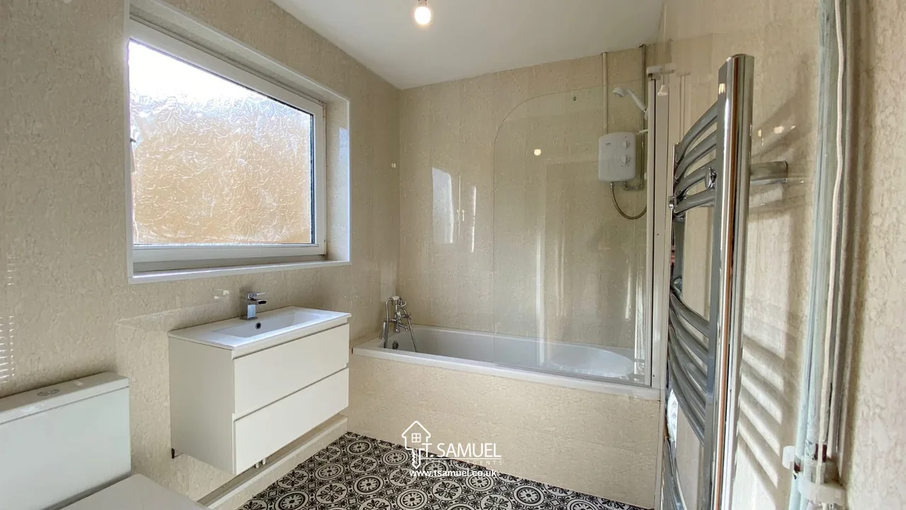 Modern bathroom with a bathtub and shower, a frosted window, white vanity with drawers, patterned floor tiles, and a towel radiator on the right wall.