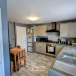 Modern kitchen with light cabinets, black appliances, a small wooden dining table with two chairs, and a window above the sink letting in natural light.