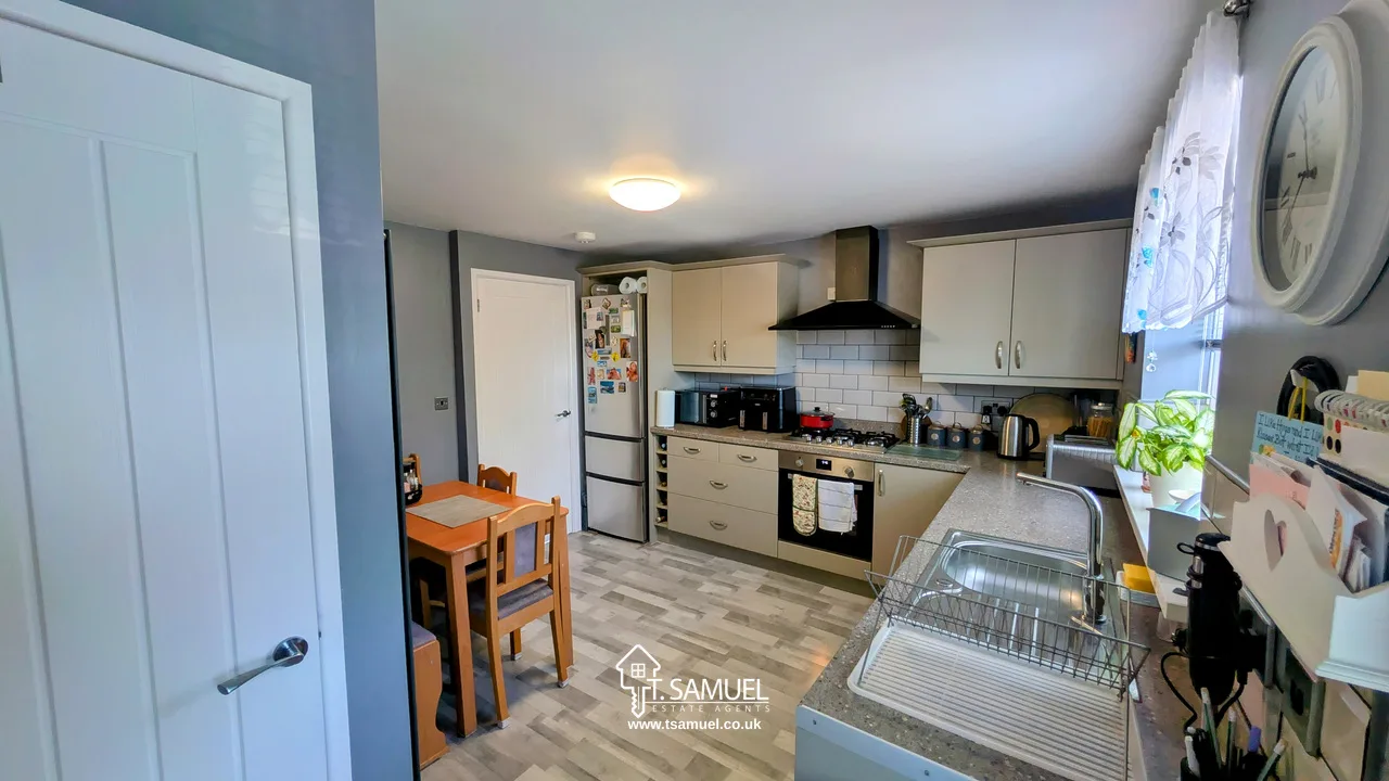Modern kitchen with light cabinets, black appliances, a small wooden dining table with two chairs, and a window above the sink letting in natural light.