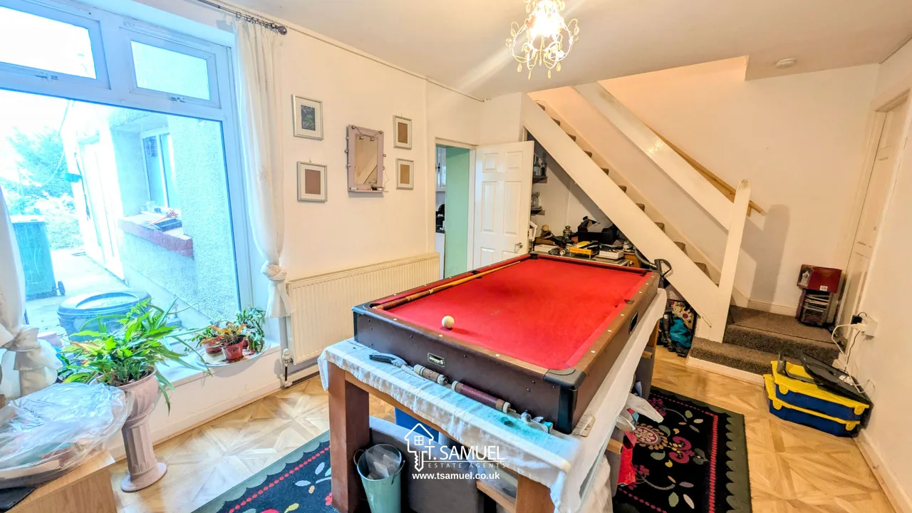 A room with a red pool table in the center, plants by a window, wall decor, a staircase, and various household items scattered around.