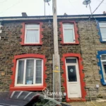 A row of terraced stone houses with red and blue window and door frames; a car is parked in front and a utility pole stands between the houses.