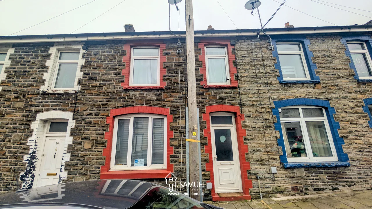 A row of terraced stone houses with red and blue window and door frames; a car is parked in front and a utility pole stands between the houses.