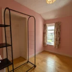 A small room with pink walls, wooden floor, a window with floral curtains, and a black open shelving unit. T. Samuel Estate Agents logo is visible in the bottom left corner.