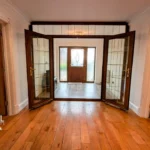 A spacious, empty room with wooden floors, glass double doors, and multiple entryways, viewed from inside. Estate agent branding is visible in the lower left corner.