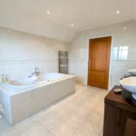 Spacious bathroom with tiled walls and floor, a bathtub, double sinks on a wooden vanity, two mirrors, and two heated towel rails.