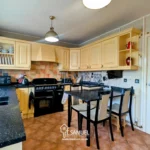 A kitchen with yellow cabinets, black countertops, a stove, microwave, dining table with four chairs, and tile flooring. A window provides natural light.